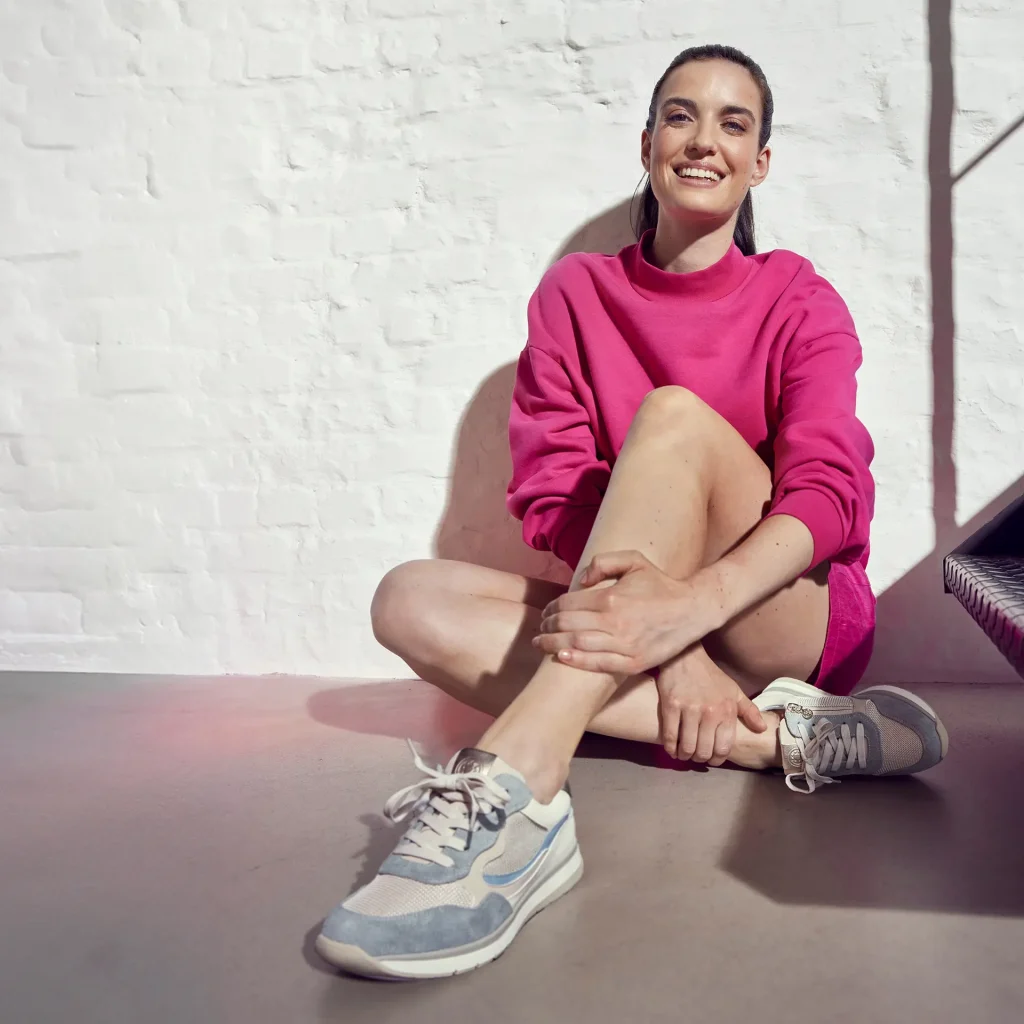Lachende Frau im pinkfarbenen Sweatshirt trägt Relife Sneaker in Grau-Blau