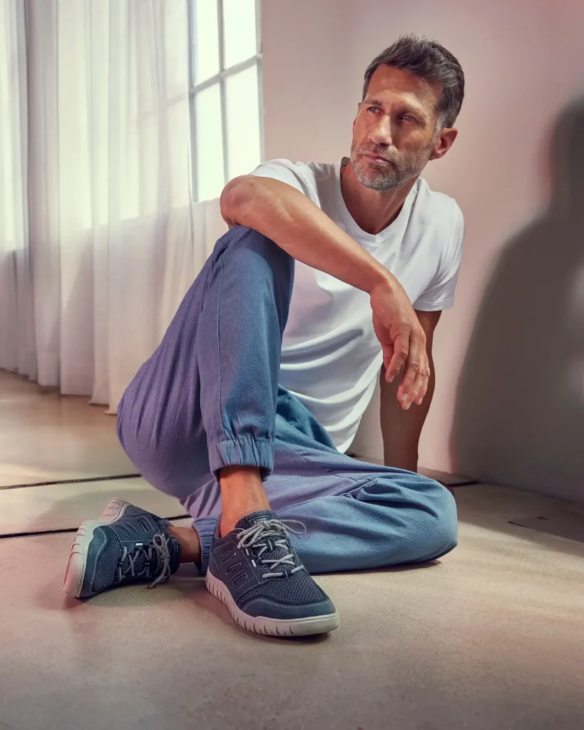 Mann sitzt auf dem Boden und trägt blaue Relife Sneaker mit weißem T-Shirt